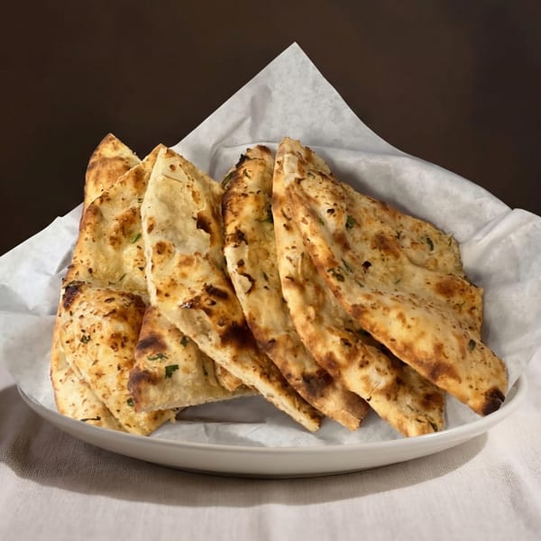 A white bowl filled with warm, golden-brown naan bread pieces, lined with white parchment paper.